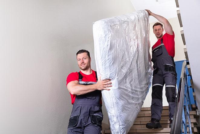 two workers carrying a heavy box spring out of a bedroom in Sharon